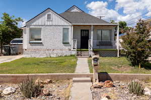 View of front of house featuring covered porch, a front yard, brick siding, roof with shingles, and board and batten siding