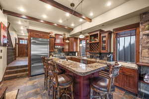 Kitchen with stainless steel appliances, stone tile floors, backsplash, beamed ceiling, and a center island