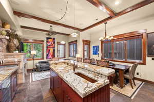 Kitchen with beam ceiling, stone tile floors, a chandelier, and light stone counters