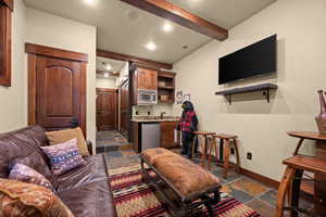 Living area featuring stone tile flooring, bar with sink, recessed lighting, and beamed ceiling