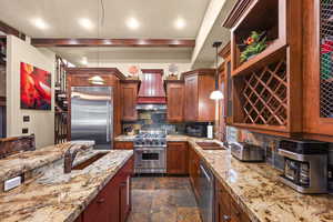 Kitchen featuring high quality appliances, custom exhaust hood, decorative backsplash, dark stone finish floors, and light stone counters