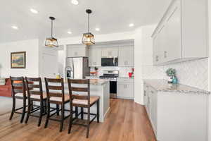Kitchen featuring stainless steel appliances, a breakfast bar, light wood finished floors, light stone countertops, and decorative backsplash