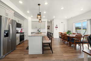 Kitchen featuring appliances with stainless steel finishes, a sink, backsplash, a center island with sink, and light stone countertops