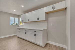 Kitchen featuring baseboards, backsplash, light wood finished floors, white cabinets, and recessed lighting
