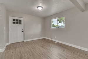 Empty room with light wood-type flooring, baseboards, and a textured ceiling
