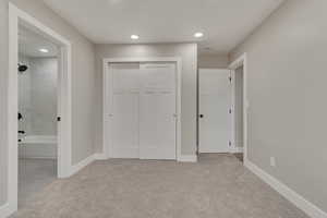 Unfurnished bedroom featuring light colored carpet, a closet, ensuite bath, recessed lighting, and baseboards