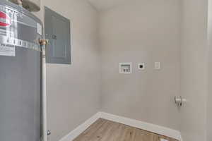 Washroom featuring hookup for an electric dryer, electric panel, baseboards, hookup for a washing machine, and light wood-type flooring