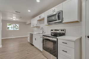 Kitchen with appliances with stainless steel finishes, a sink, baseboards, light countertops, and recessed lighting