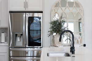 Kitchen view of stainless steel fridge, a sink, tasteful backsplash, light countertops, and white cabinets