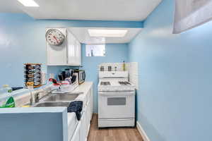 Kitchen with white range with gas cooktop, light wood-style flooring, white cabinetry, a sink, and light countertops