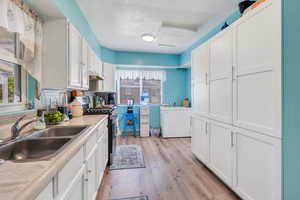 Kitchen featuring stainless steel gas stove, a sink, light wood-style flooring, white cabinetry, and light countertops