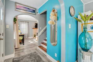 Entrance foyer featuring arched walkways, wood finished floors, crown molding, baseboards, and stairway