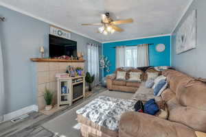 Living room featuring a textured ceiling, wood finished floors, a ceiling fan, crown molding, and a glass covered fireplace