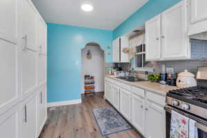 Kitchen with stainless steel range with gas cooktop, a sink, light countertops, decorative backsplash, and white cabinets