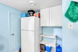 Kitchen featuring freestanding refrigerator, white cabinets, light countertops, and a textured ceiling