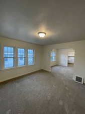 Carpeted spare room featuring a textured ceiling and baseboards