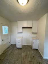 Kitchen featuring wood tiled floors, white cabinetry, baseboards, a textured ceiling, and light countertops