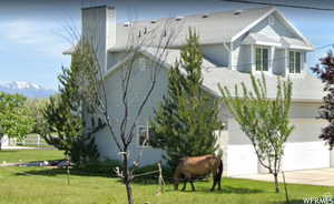 View of side of home with concrete driveway, a lawn, a chimney, an attached garage, and a shingled roof