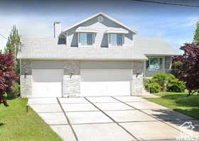 View of front facade with stone siding, a garage, concrete driveway, a front yard, and a chimney