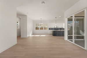 Unfurnished living room featuring a chandelier, baseboards, light wood-style flooring, and recessed lighting