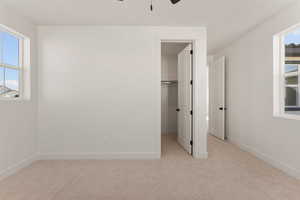 Unfurnished bedroom with a spacious closet, light colored carpet, baseboards, and ceiling fan