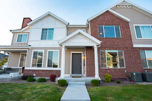 View of property featuring brick siding, cooling unit, board and batten siding, and a front yard