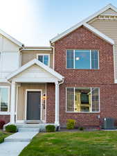 View of front of house featuring central AC unit, brick siding, and a front lawn