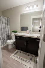 Full bath with vanity, toilet, wood finished floors, and a shower with shower curtain