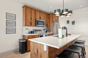 Kitchen with stainless steel appliances, light wood-style floors, brown cabinets, a sink, and recessed lighting