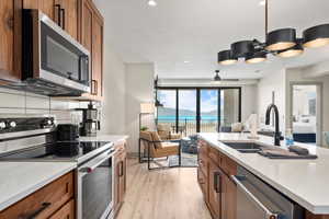 Kitchen featuring appliances with stainless steel finishes, a sink, open floor plan, brown cabinets, and light wood-style flooring