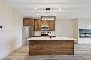 Kitchen with brown cabinetry, tasteful backsplash, appliances with stainless steel finishes, a center island with sink, and hanging light fixtures