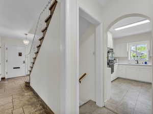 Hallway with arched walkways, baseboards, a sink, and stairs