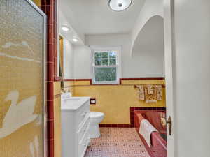 Bathroom with tile walls, vanity, a wainscoted wall, toilet, and a stall shower