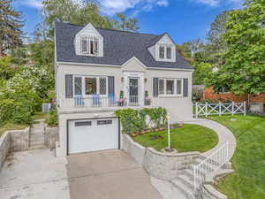 Cape cod-style house with a shingled roof, concrete driveway, an attached garage, central AC, and stairs
