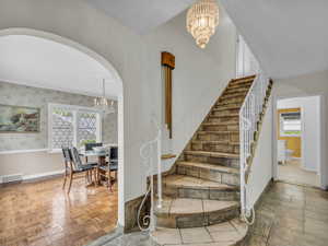 Staircase with a chandelier, baseboards, and arched walkways