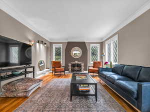 Living area with wood finished floors, crown molding, a large fireplace, and baseboards