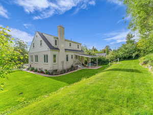 Back of property featuring a chimney, a patio, and a lawn