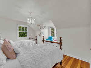 Bedroom featuring wood-type flooring, multiple windows, baseboards, a chandelier, and vaulted ceiling