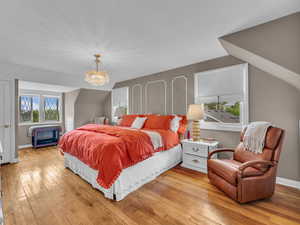 Bedroom featuring light wood-style flooring, a chandelier, baseboards, and lofted ceiling