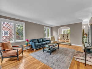 Living area with arched walkways, light wood-style flooring, crown molding, and baseboards