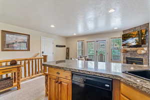 Kitchen with black dishwasher, light carpet, a textured ceiling, a fireplace, and a sink