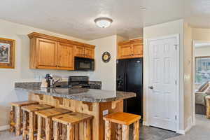 Kitchen with black appliances, a sink, a kitchen breakfast bar, baseboards, and a peninsula