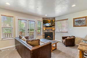 Living area with light colored carpet, a stone fireplace, baseboards, a textured ceiling, and plenty of natural light