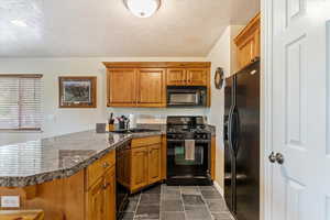 Kitchen featuring black appliances, a peninsula, dark countertops, brown cabinets, and a textured ceiling