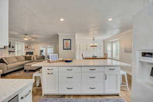 Kitchen featuring ornamental molding, a breakfast bar area, light wood-style floors, white cabinets, and white refrigerator with ice dispenser