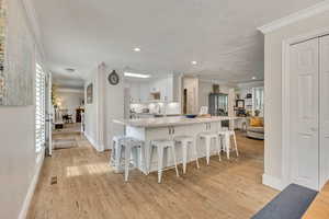 Kitchen with crown molding, a kitchen bar, light wood-style floors, white cabinetry, and baseboards