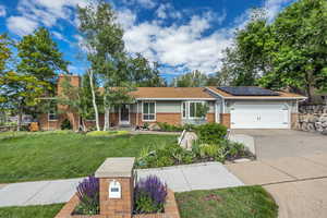Ranch-style home with brick siding, solar panels, driveway, a front lawn, and a garage