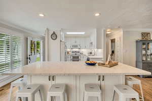 Kitchen with white appliances, light wood-style floors, light stone countertops, crown molding, and a textured ceiling