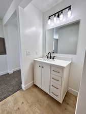 Bathroom with wood finished floors, electric panel, vanity, and baseboards