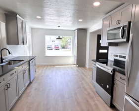 Kitchen featuring appliances with stainless steel finishes, a sink, dark countertops, a textured ceiling, and light wood-type flooring